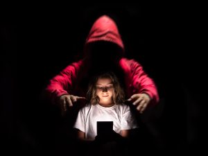 “Vulnerable child engrossed in smartphone as a dark hooded predator looms behind — powerful visual warning of online threats and the urgent need to protect children from digital dangers.”
