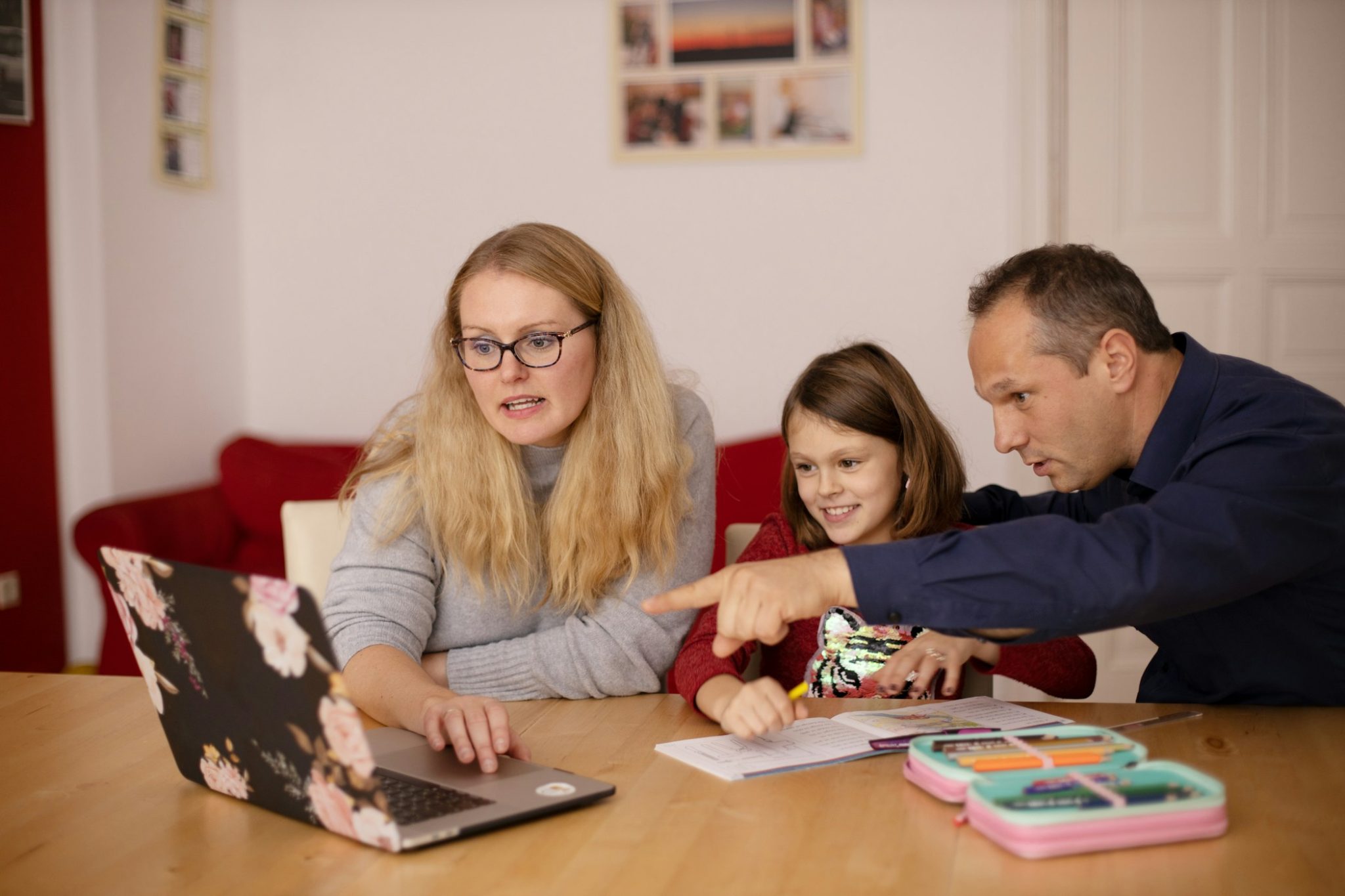 A mother, father, and young daughter sit together at a kitchen table using a laptop for schoolwork. The parents point at the screen while the daughter smiles, showing family engagement in online learning. Gigabit IQ is helping protect the family’s digital space and keeping children safe in education.